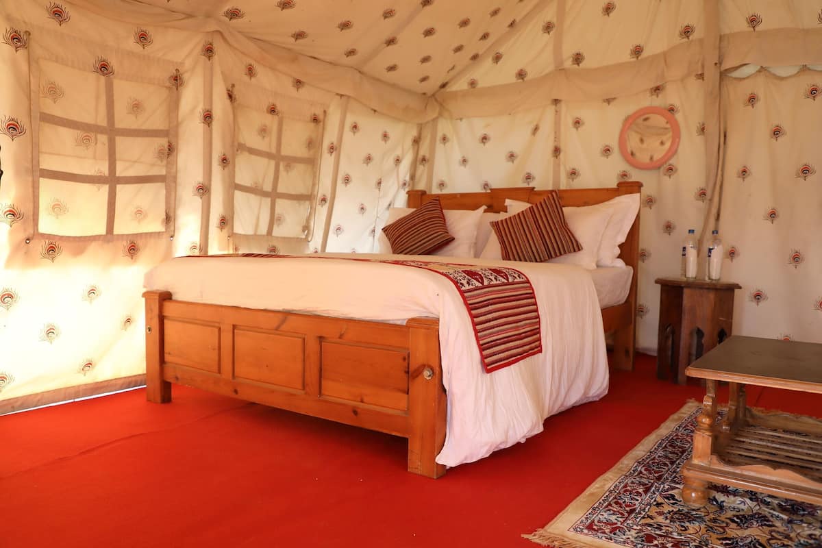 A wooden bed with a white bedspread and red accents, a small wooden nightstand, and a patterned rug.
