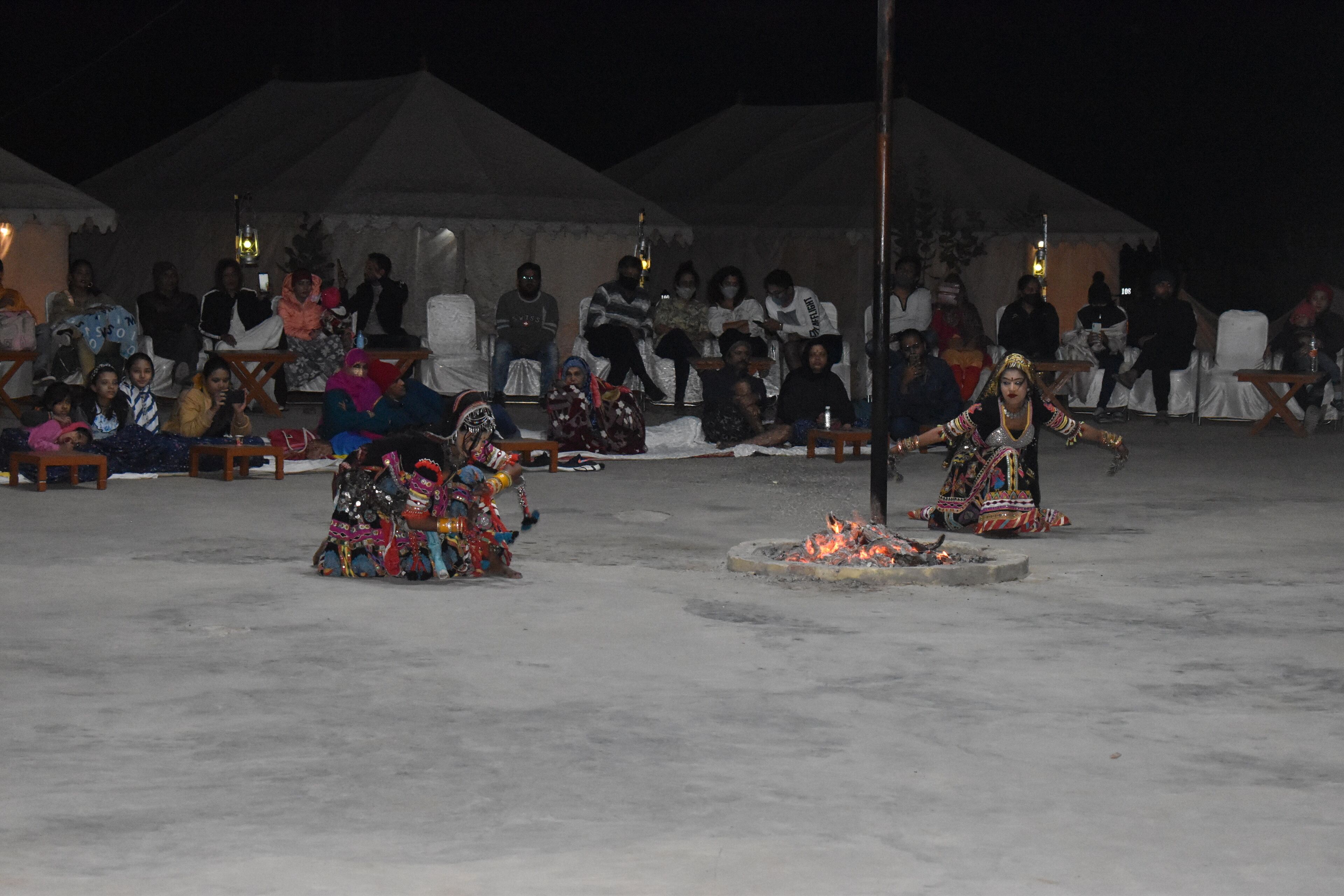 Un grupo de personas con atuendo tradicional actuando en un espacio abierto con fuego en el centro, bajo una estructura cubierta.