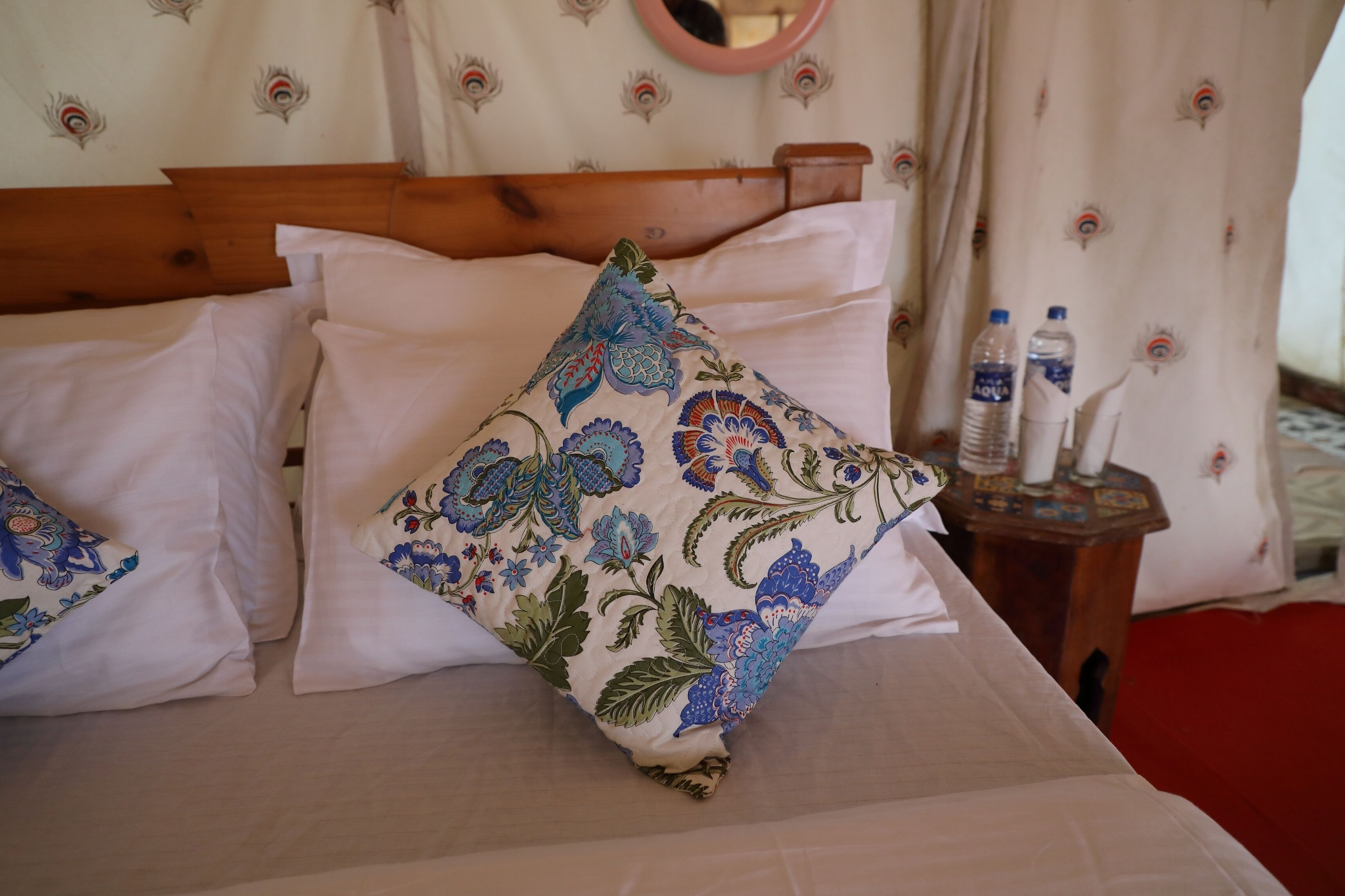 Een bed met witte lakens, een houten hoofdbord en een sierkussen met bloemenprint.