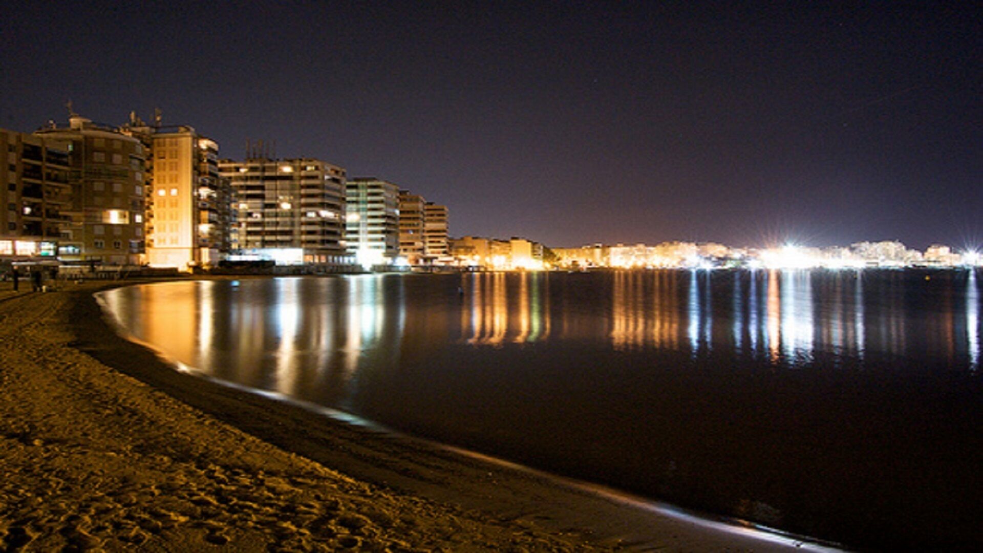 A nighttime beach scene with buildings along the shore.