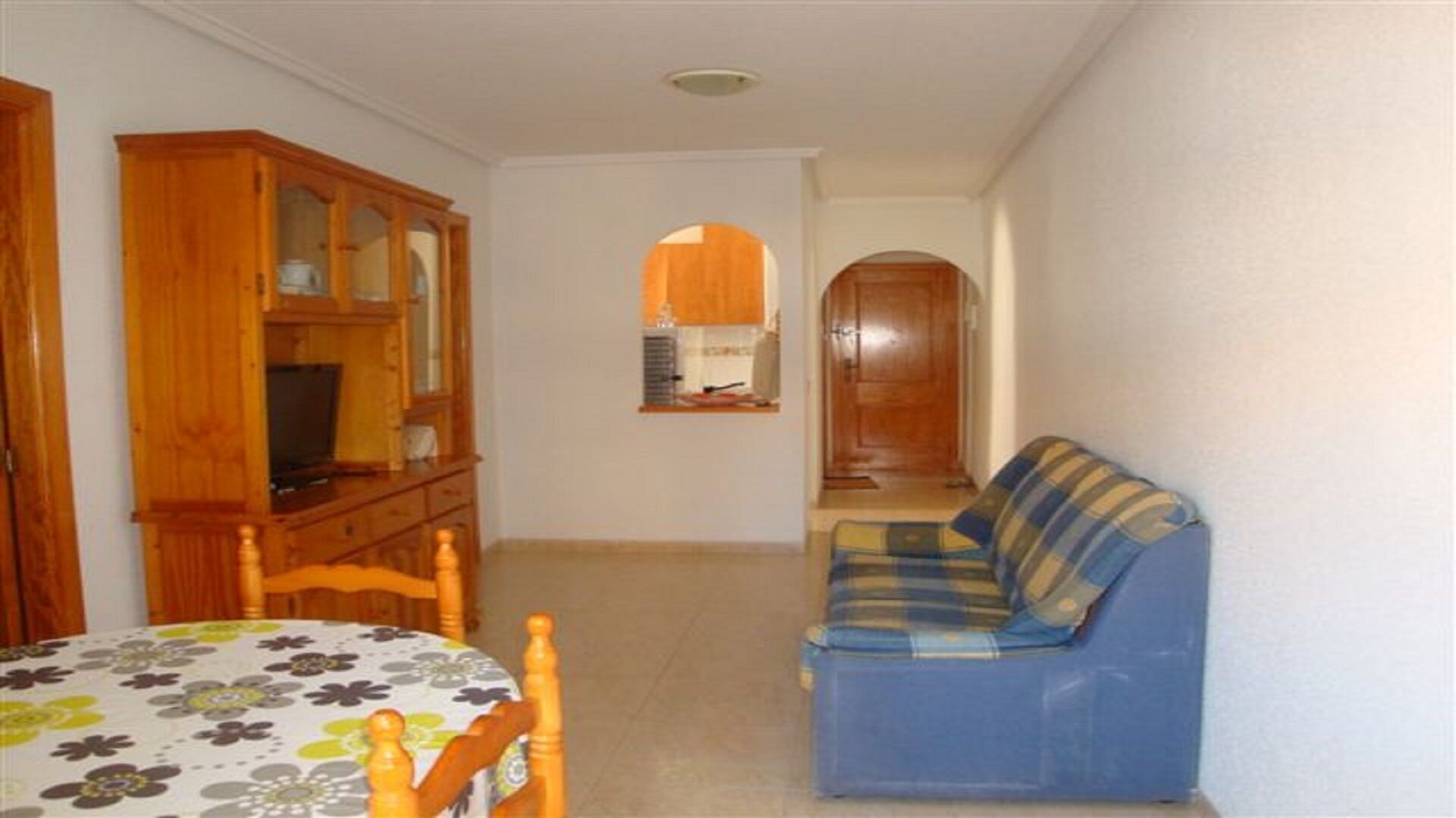 A hallway with a dining table, a blue sofa, and wooden cabinets.