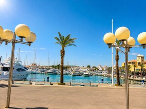 A marina with boats docked, palm trees, and a clear blue sky.