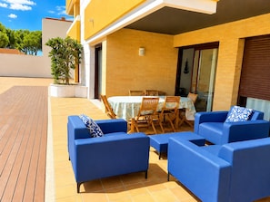 Eine Terrassengruppe im Freien mit blauen Sofas und einem Tisch, einem Fliesenboden und einem gelben Gebäude mit Backsteinmauer.