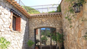 Une cour dallée de pierres, avec un sol carrelé, des plantes en pot et une rambarde métallique donnant sur une colline.