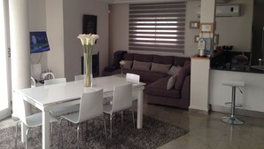 Un salon moderne comprenant une table à manger, des chaises, un canapé et un téléviseur fixé au mur.