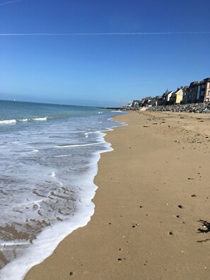 A sandy beach with waves lapping at the shore, a rocky breakwater, and buildings along the coastline.
