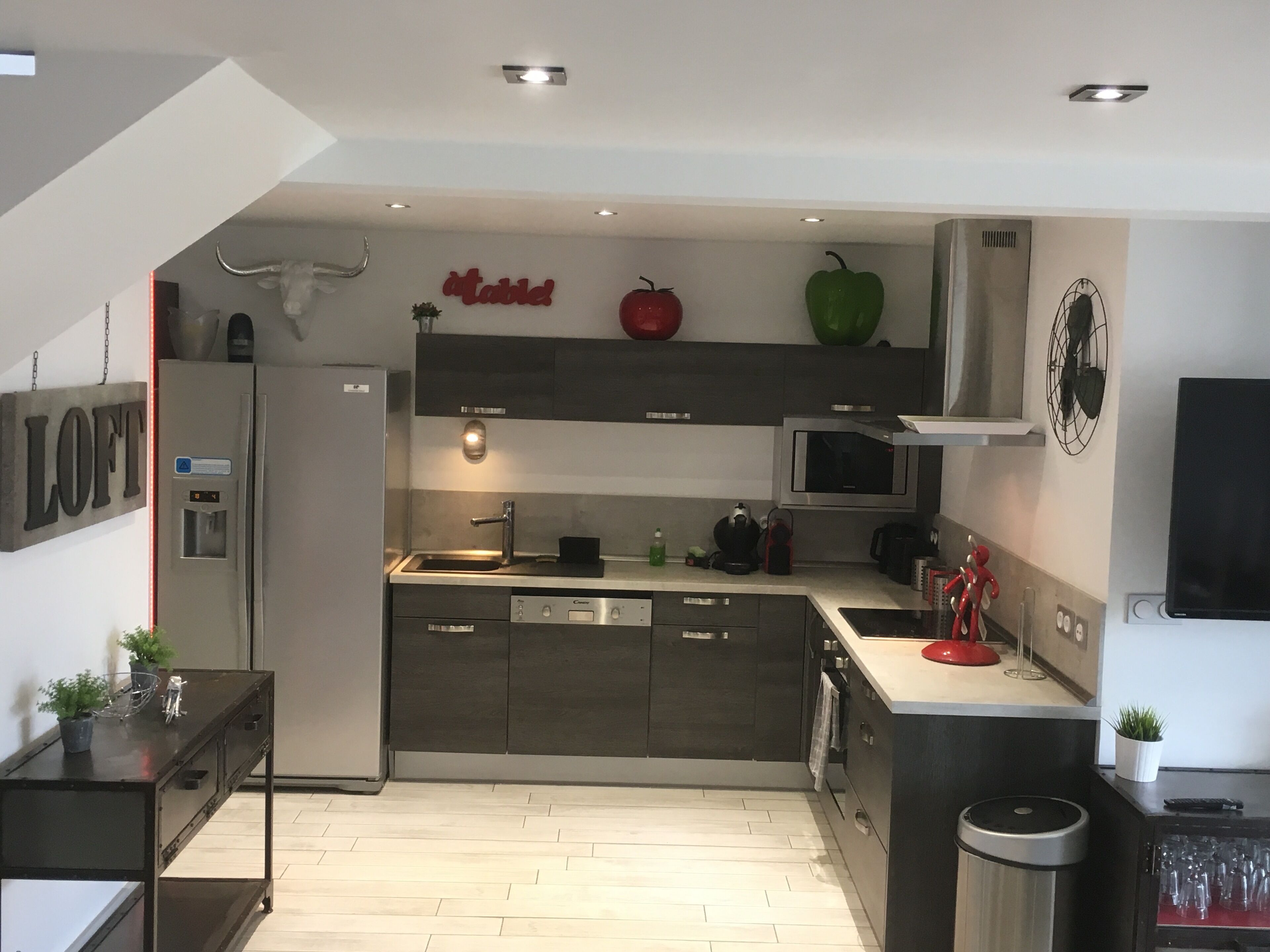 A modern kitchen with a built-in oven, microwave, and sink. There is a refrigerator, a coffee machine, and a trash bin.
