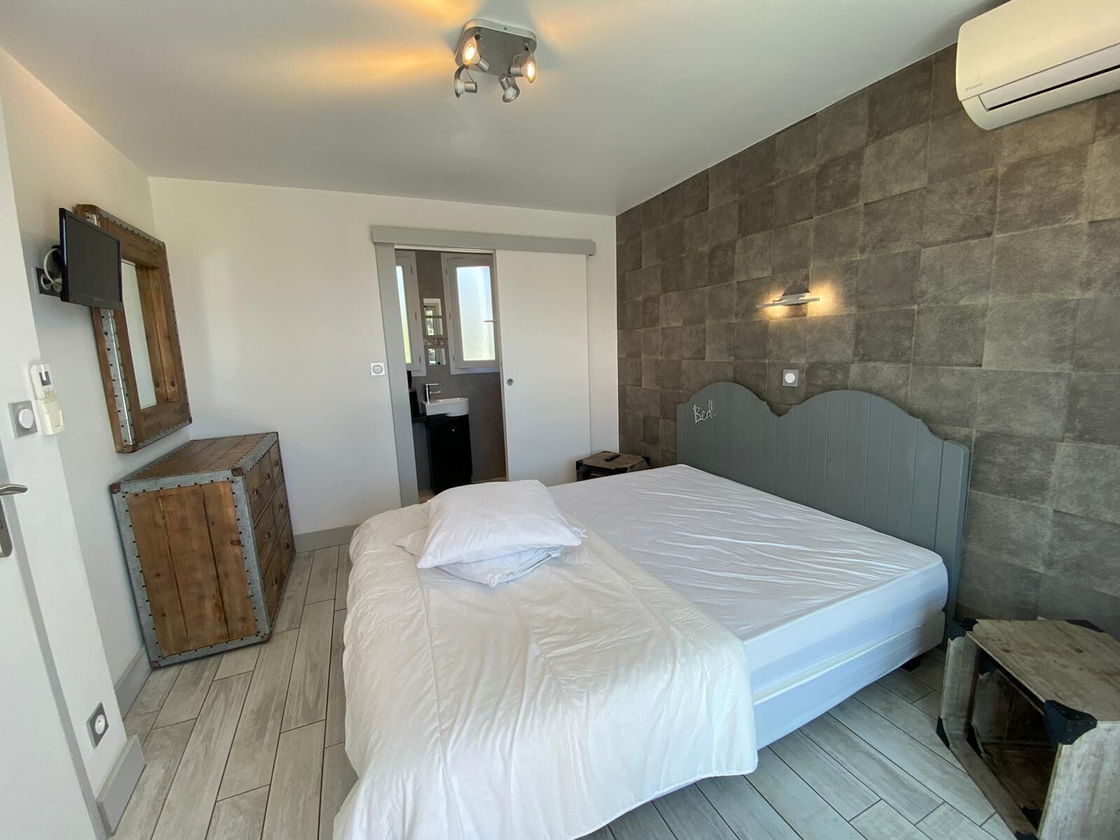 Quarto com uma cama grande, um armário de madeira, um espelho, uma TV na parede e um aparelho de ar condicionado.