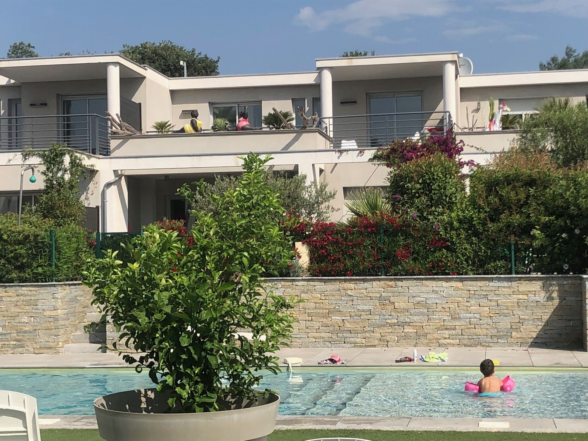 Un edificio moderno con piscina, rodeado de vegetación y muros de piedra.