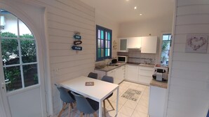 A compact kitchen with white cabinets, a dining area with a table and chairs, a window with colorful stained glass, and a small island with a sink and microwave. - Quiet Capbreton house at the marina, between beaches and amenities (Capbreton)