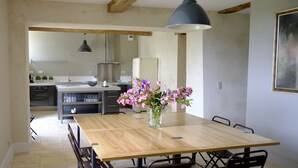 A dining area with a wooden table, black chairs, a vase of flowers, and a hanging pendant light. - Maison de Maître 12 pers / private pool - Biran- GERS  (Biran)