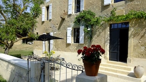 A stone building with white shutters, a potted red flower, and a metal gate. - Maison de Maître 12 pers / private pool - Biran- GERS  (Biran)