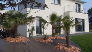 A modern two-story house with a balcony, surrounded by tropical plants and a well-maintained lawn. - Comfortable guest room "les Bruyères" in the rising sun (Bruc-Sur-Aff)