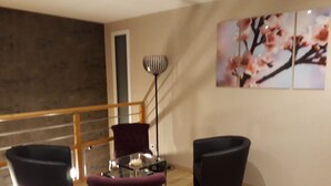 A modern living room with a glass coffee table, two black armchairs, a purple chair, a floor lamp, and a staircase. - Comfortable guest room "les Bruyères" in the rising sun (Bruc-Sur-Aff)