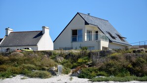 Una casa moderna con techo inclinado, ventanas grandes y un patio cercado con rocas y vegetación.