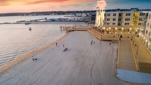Una playa con un muelle de madera que se adentra en el agua, un edificio con balcones y un cielo despejado.