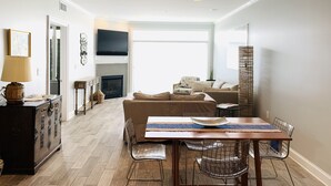 Una sala de estar moderna con chimenea, un comedor con mesa de madera y sillas metálicas, y un sofá.
