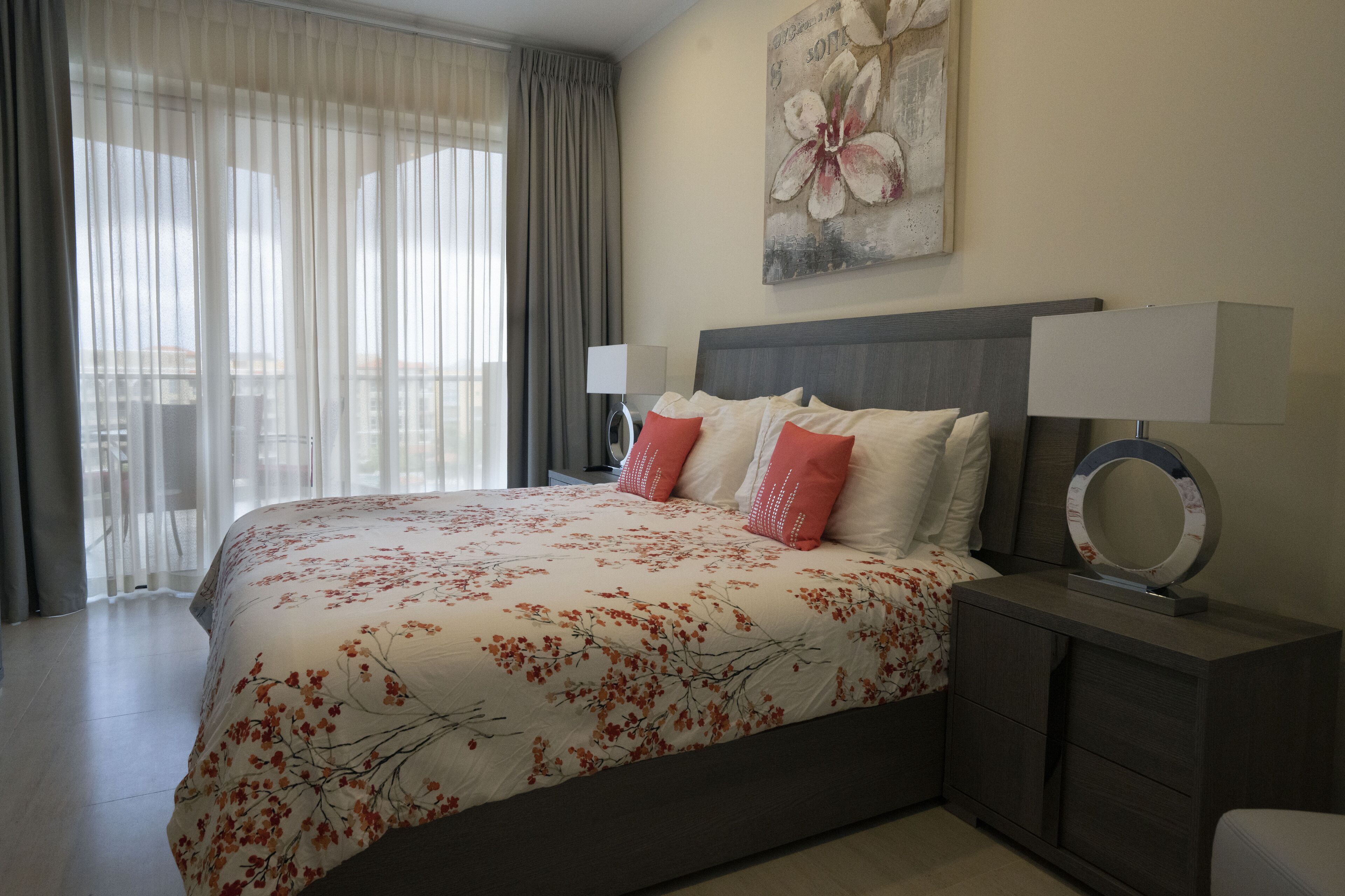 Une chambre d’hôtel avec un grand lit, une table de chevet avec une lampe, un miroir et une œuvre d’art florale accrochée au mur.