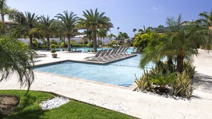 Zona de piscina con sillas de descanso, palmeras y un cielo azul despejado.