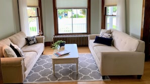Een woonkamer met twee beige banken, een witte salontafel en een kroonluchter.
