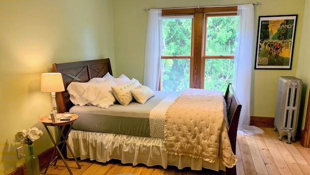 Een slaapkamer met houten vloer, een bed met wit- en groen beddengoed, een nachtkastje met lamp, een radiator, en een poster aan de muur.