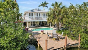 Une maison à deux étages avec une piscine, entourée d’une végétation luxuriante et de palmiers.