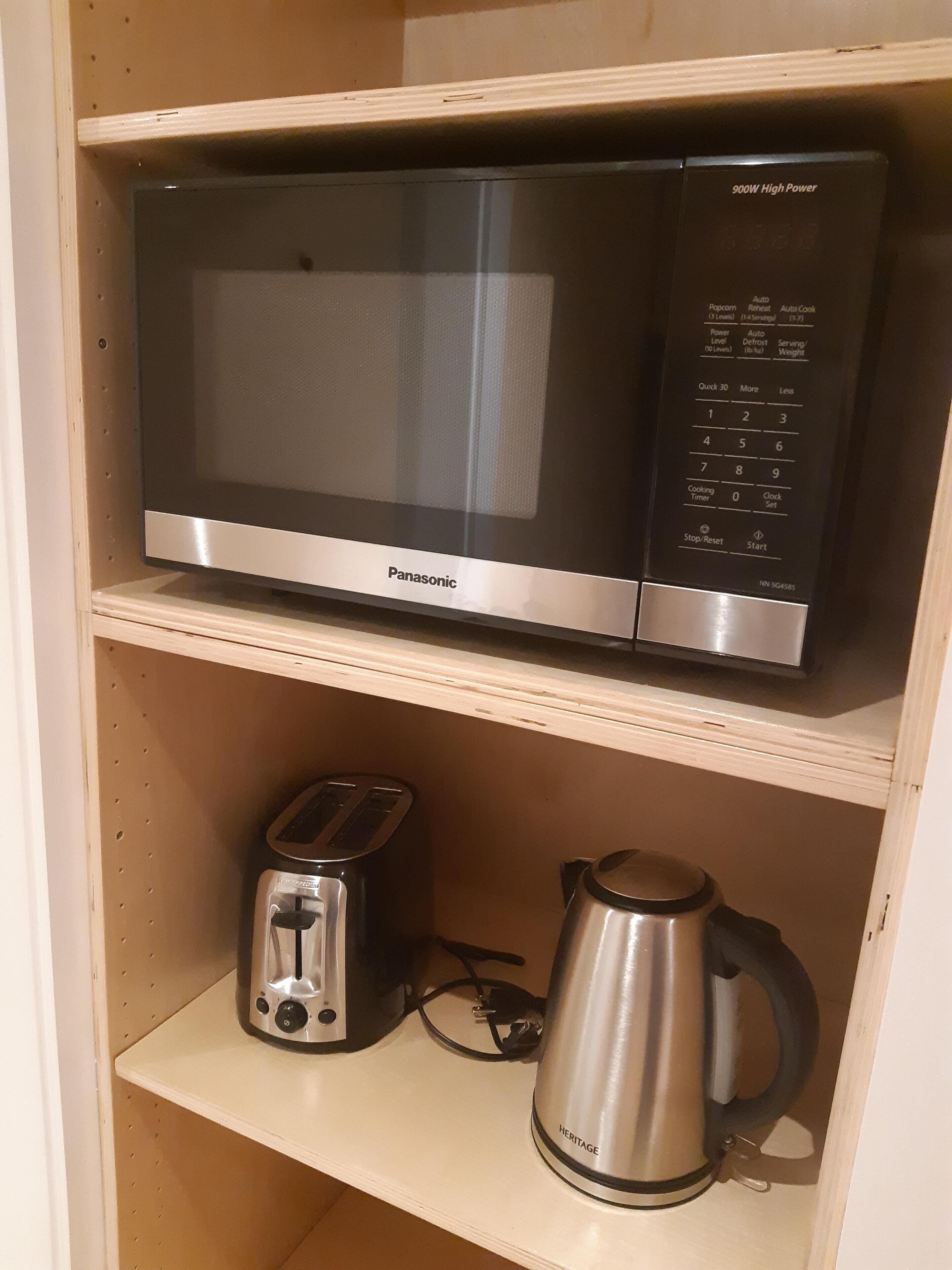 A Panasonic microwave oven on a shelf with a toaster and a stainless steel kettle below it.