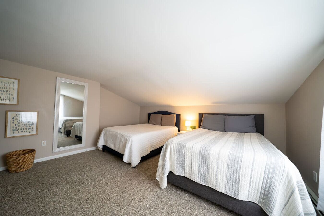 Une chambre avec deux lits simples, un grand miroir et une petite table de chevet avec une lampe.