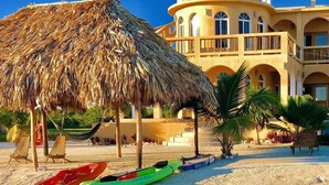 Una playa con sombrilla de paja, piscina y un edificio con balcones.