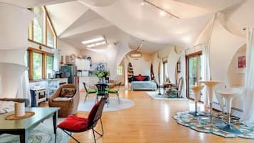 Un vaste espace de vie doté d’un haut plafond, comprenant une table à manger, des chaises, un canapé et un coin cuisine visible au fond.