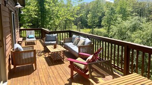 Um deck de madeira com móveis de exterior, incluindo um sofá e cadeiras, com vista para uma área arborizada.