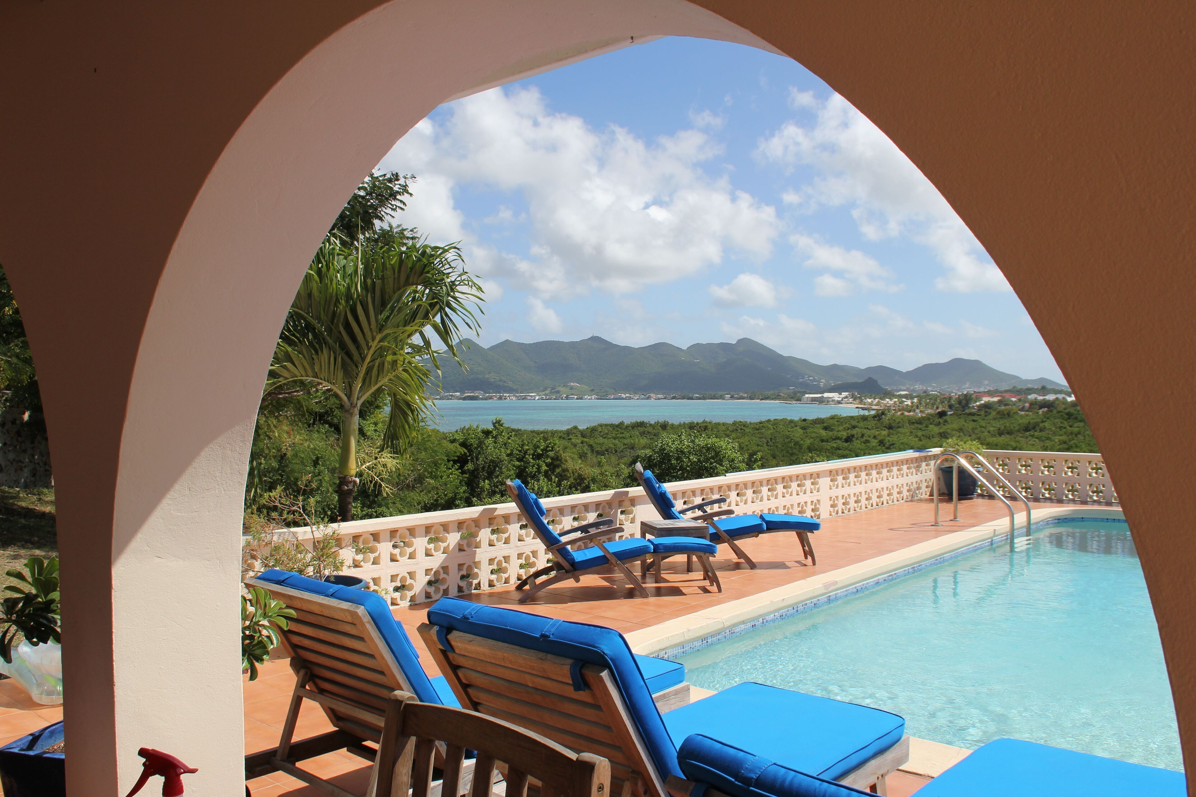 A pool area with lounge chairs and a view of the ocean and mountains.