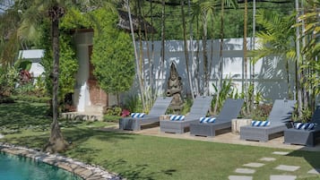 A poolside area with lounge chairs, a stone statue, and lush greenery.