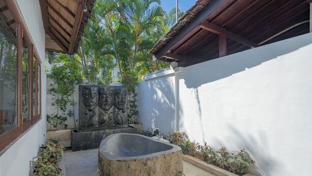 Un recipiente de hormigón en un patio con pared blanca, techo de madera y plantas tropicales.