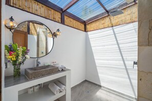Une salle de bain avec un lavabo en pierre, un miroir et un plafond en bambou.