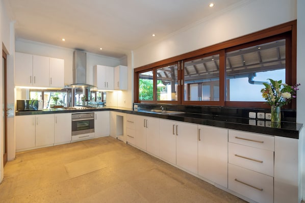 A modern kitchen with white cabinets, a stainless steel range hood, and a large window with wooden framing.