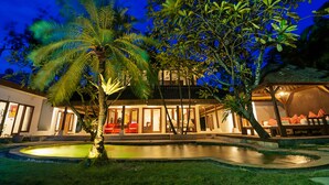 Un resort bien iluminado con piscina, palmeras y una zona de estar techada.