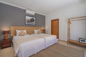 A double bed with a wooden headboard, two bedside tables, a wall-mounted air conditioner, a framed picture, a wooden wardrobe, and a radio on a shelf.