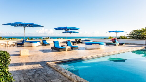 A poolside area with lounge chairs and umbrellas, a clear view of the ocean, and a tiled pool. - 1 BD,1.5 Bathroom, Beautiful Condo (Providenciales)
