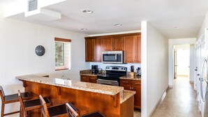 A modern kitchen with granite countertops, wooden cabinets, and a central island with bar stools. - 1 BD,1.5 Bathroom, Beautiful Condo (Providenciales)
