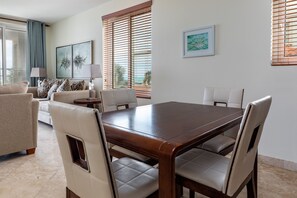 A dining area with a wooden table and four chairs, a sofa, a lamp, and a window with blinds. - 1 BD,1.5 Bathroom, Beautiful Condo (Providenciales)