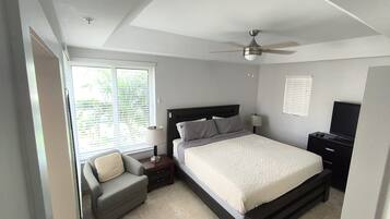 Une chambre à coucher comprenant un lit, une chaise, une table de chevet, un téléviseur et un ventilateur de plafond.