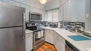 Una cocina moderna con electrodomésticos de acero inoxidable, armarios blancos, microondas, estufa y lavavajillas.