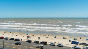 Ein Strand mit Personen, Sonnenschirmen und Autos am Ufer.