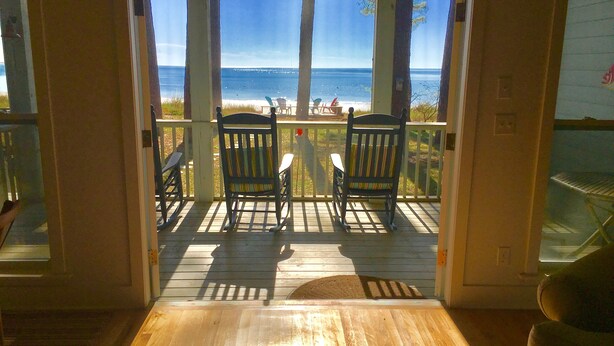 Une terrasse en bois avec deux fauteuils à bascule donnant sur une plage.