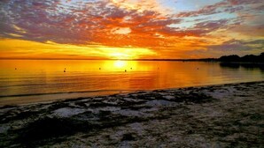 Un coucher de soleil sur une étendue d’eau calme, bordée d’une plage de sable.