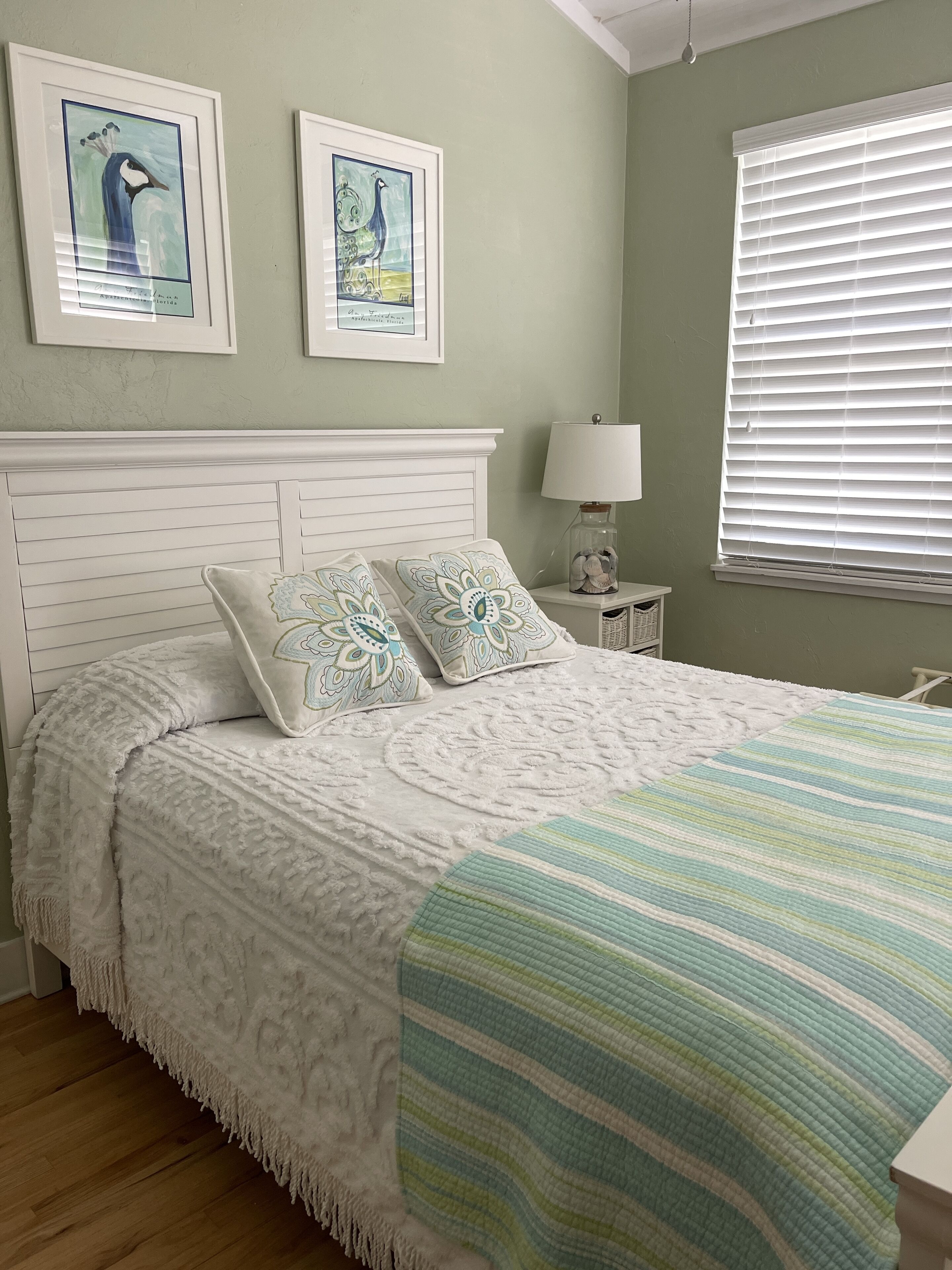 Une chambre à coucher avec une tête de lit blanche, deux coussins décoratifs, une couverture à rayures et deux œuvres d’art encadrées accrochées au mur.