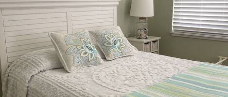 Une chambre à coucher avec une tête de lit blanche, deux coussins décoratifs, une couverture à rayures et deux œuvres d’art encadrées accrochées au mur.