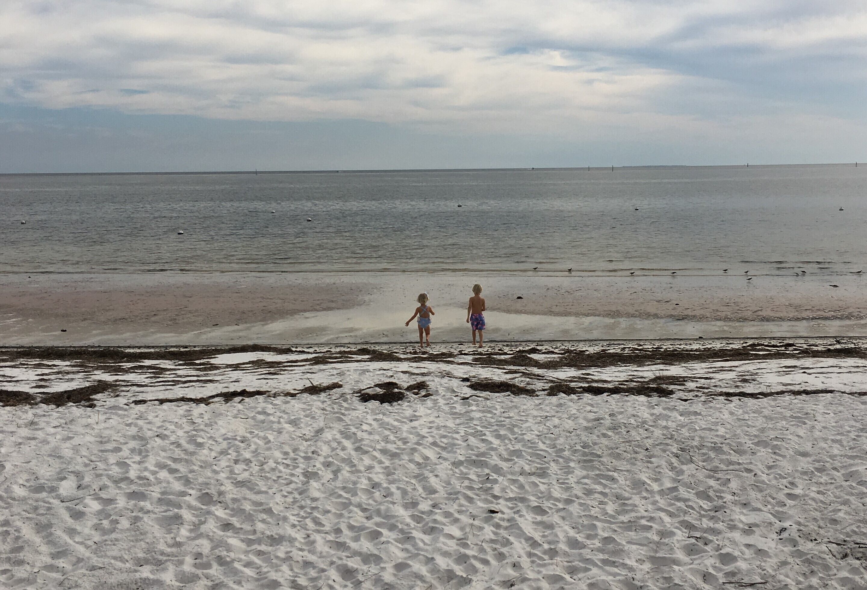 Una playa con dos personas caminando hacia el agua.