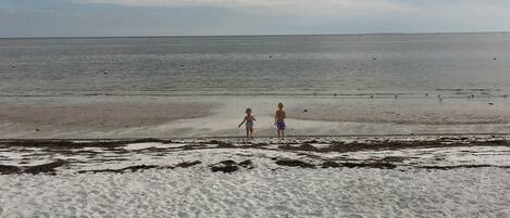 Una playa con dos personas caminando hacia el agua.